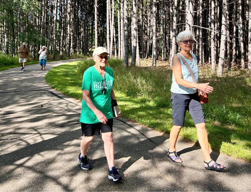 older-women-walking-together-on-paved-trail-through-pine-forest